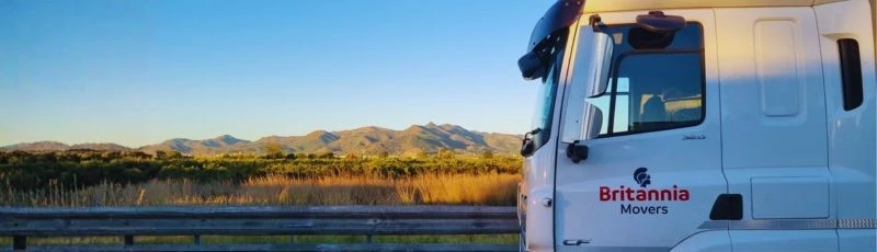 A Britannia Robbins truck in a sunny and mountainous European landscape delivering part load removals
