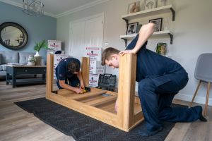Uniformed Britannia removals crew dismantle a table to prepare it for a move to France